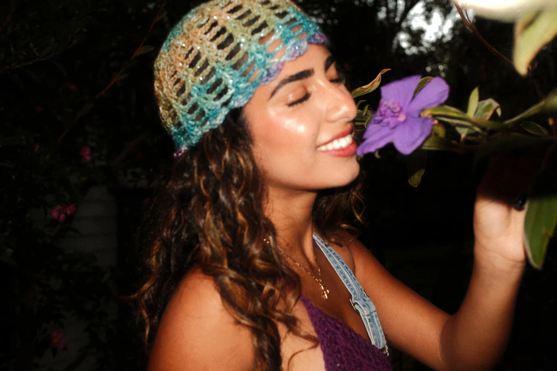 Smiling portrait with a purple garden flower and colorful crochet headpiece